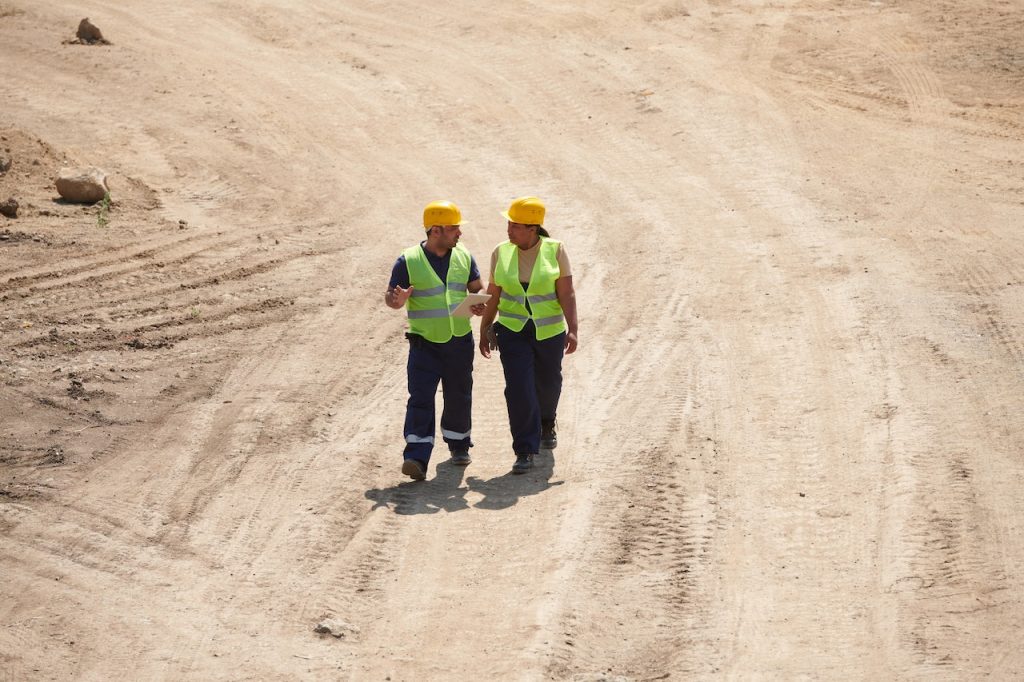 people in a safety vest and hat walking in a job site